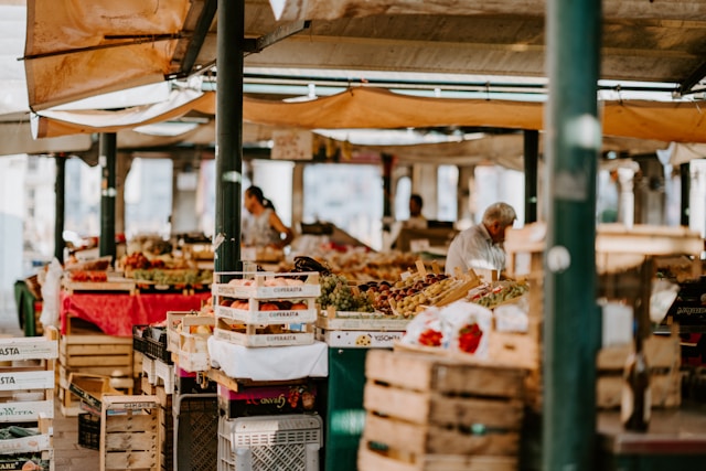 Marché provençal en plein air sous les platanes : cagettes de fruits et légumes frais
